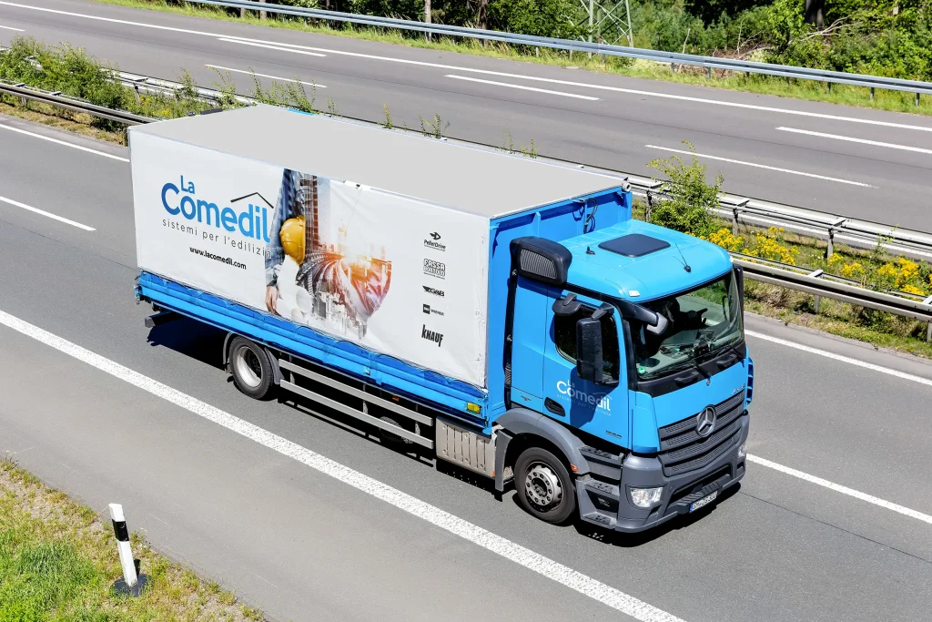 Camion La Comedil azzurro con logo su fianco in corsia autostradale.